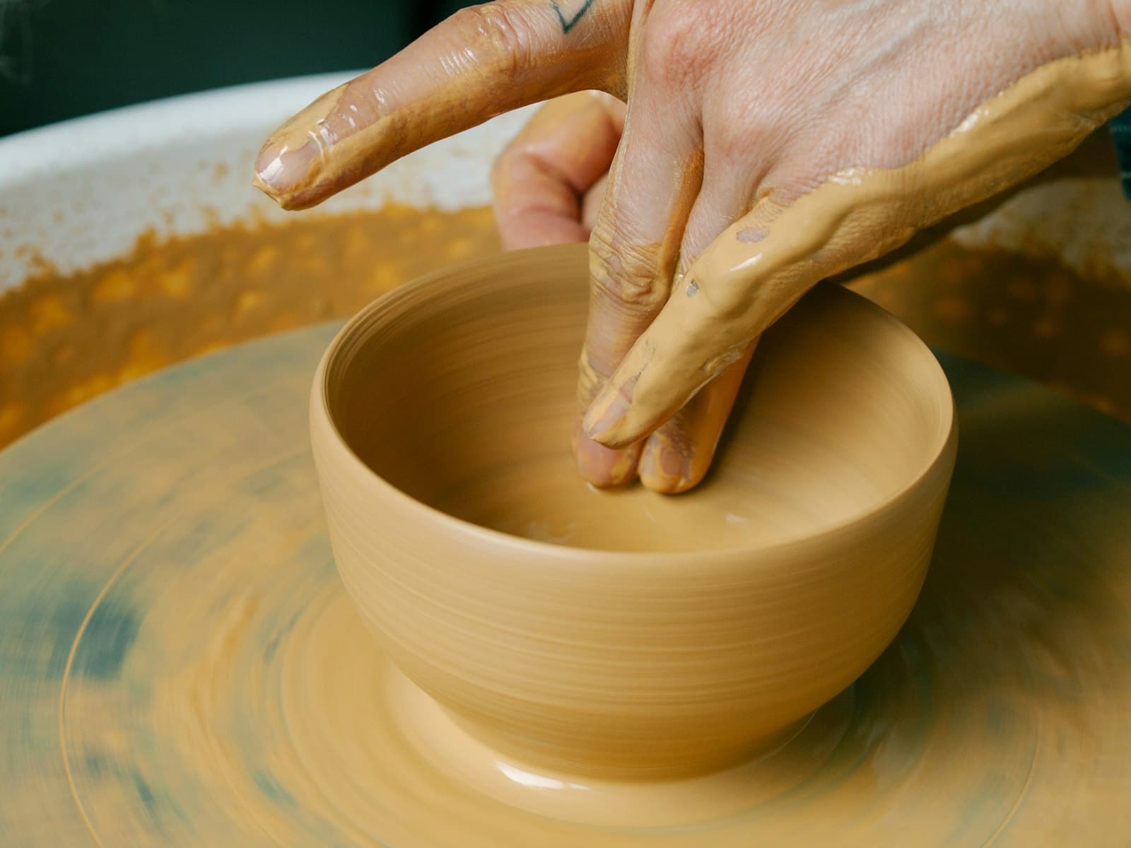A potter's hands shaping a clay bowl on the wheel