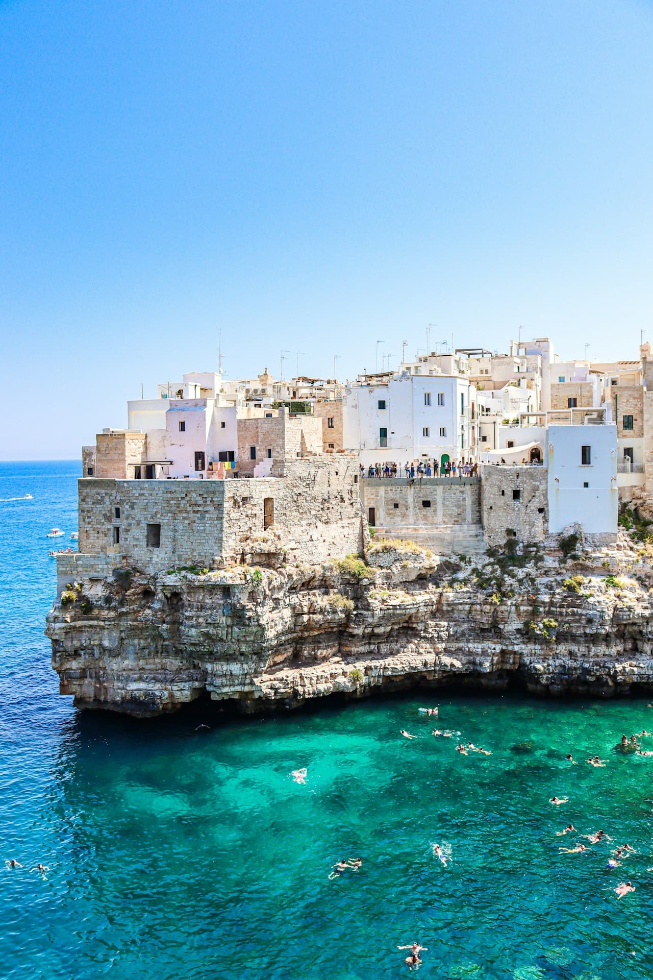 Whitewashed Polignano a Mare on the cliffs above a turquoise Adriatic cove, swimmers in the water below