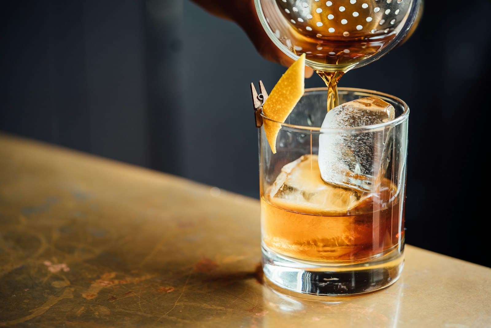 A cocktail being strained into a glass on a brass bar