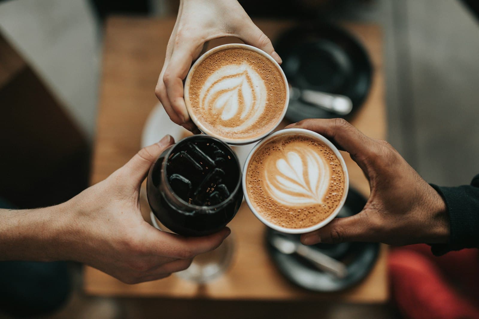 Hands bringing three coffees together over a café table