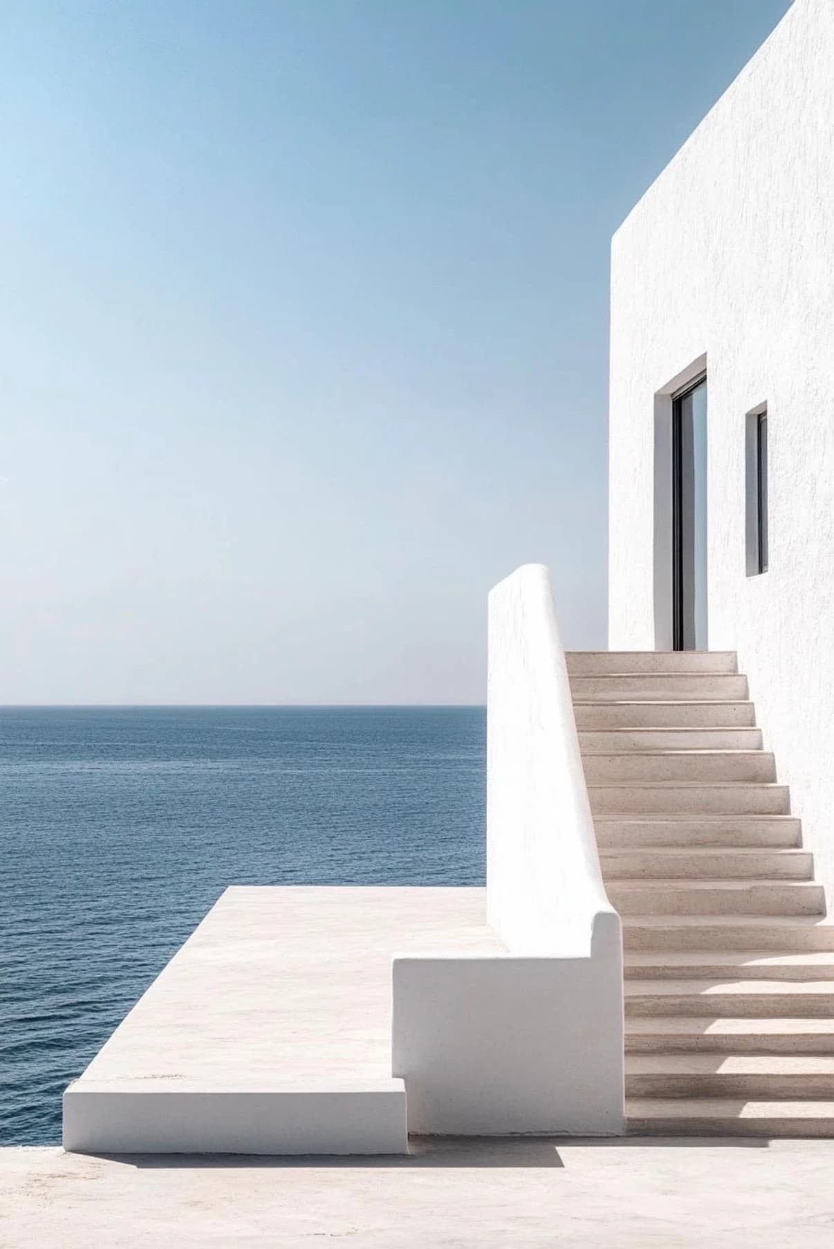 A minimal whitewashed villa with a stone staircase and terrace overlooking a calm blue Mediterranean sea