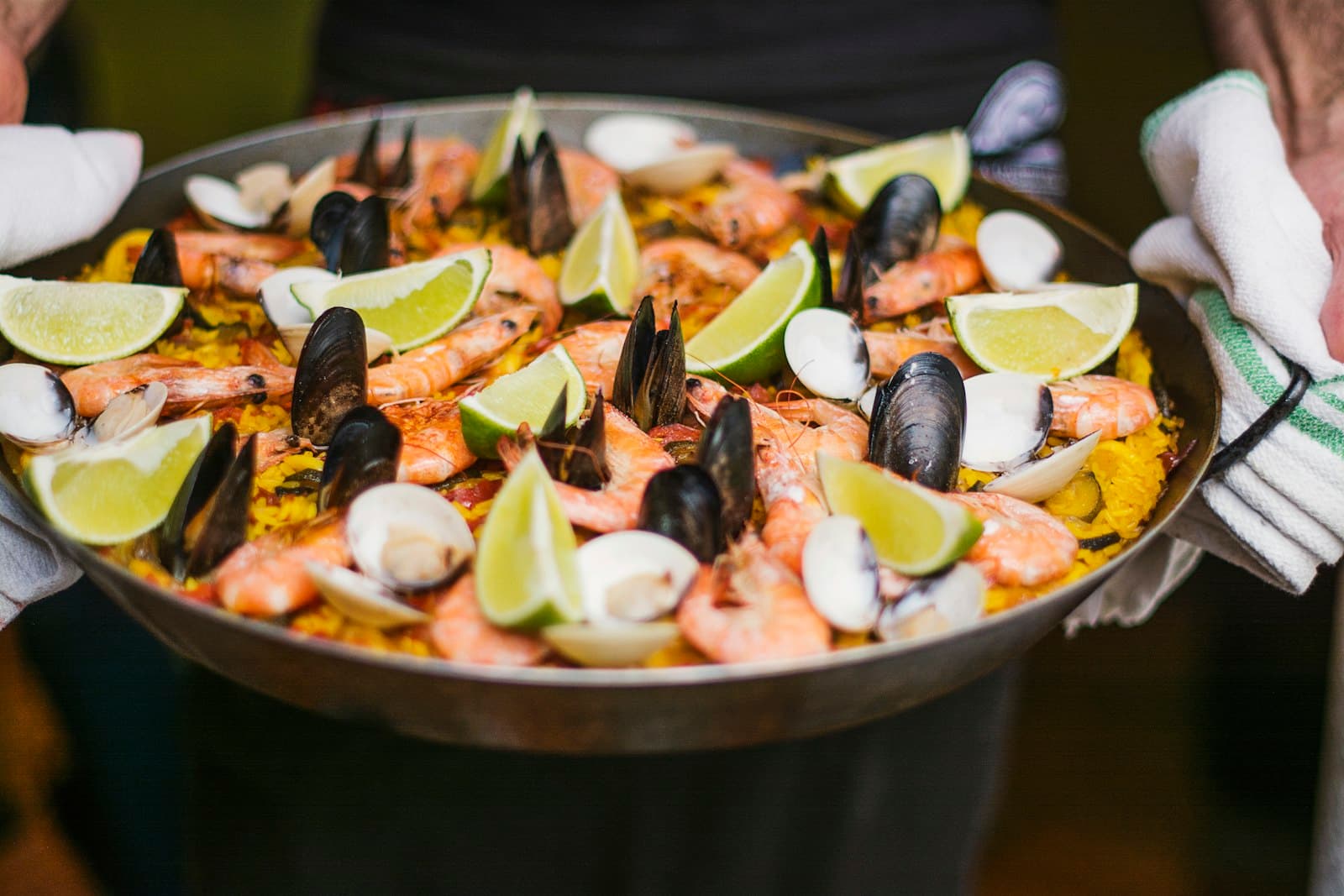 A paella pan of seafood and rice carried to the table