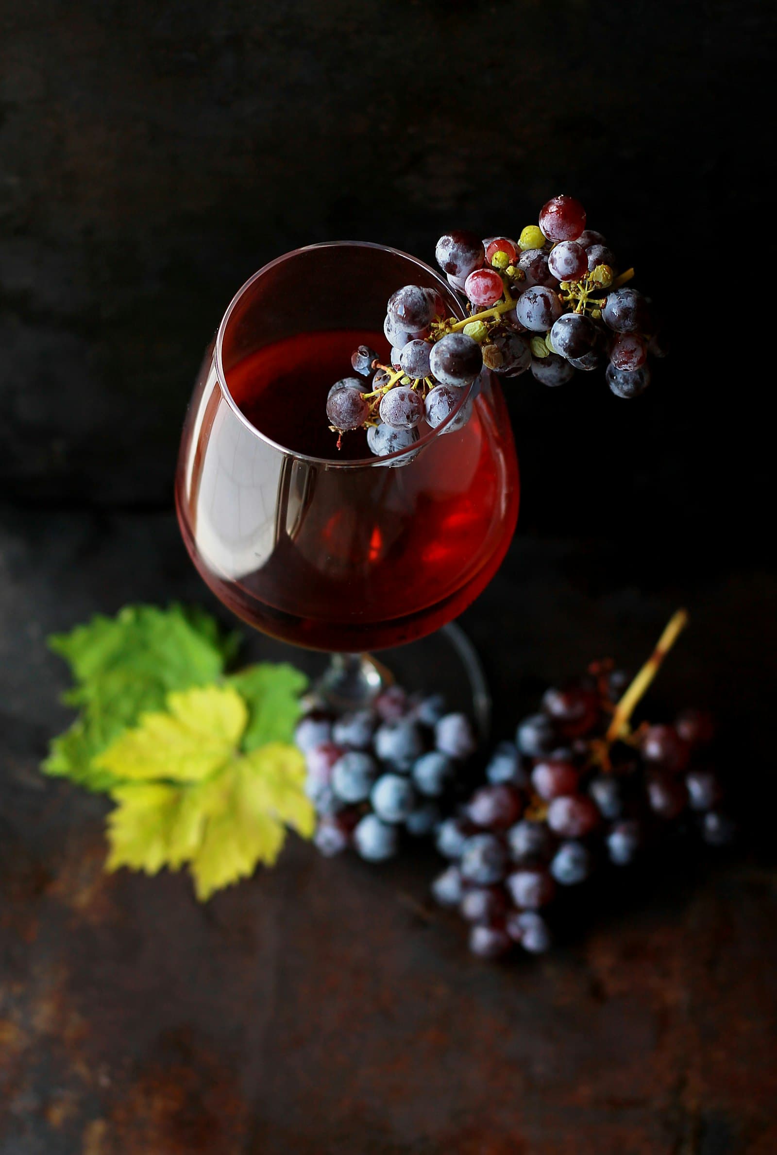 Moody still life of a wine glass draped with dark grapes