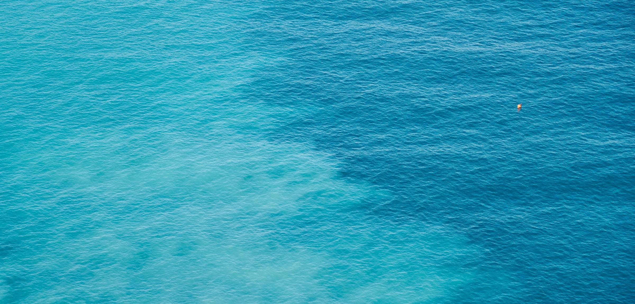 Clear Mediterranean water seen from above, turquoise shallows dissolving into deep blue